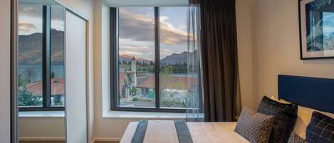 A hotel room with a large bed, a view of mountains and a lake, and a modern design.