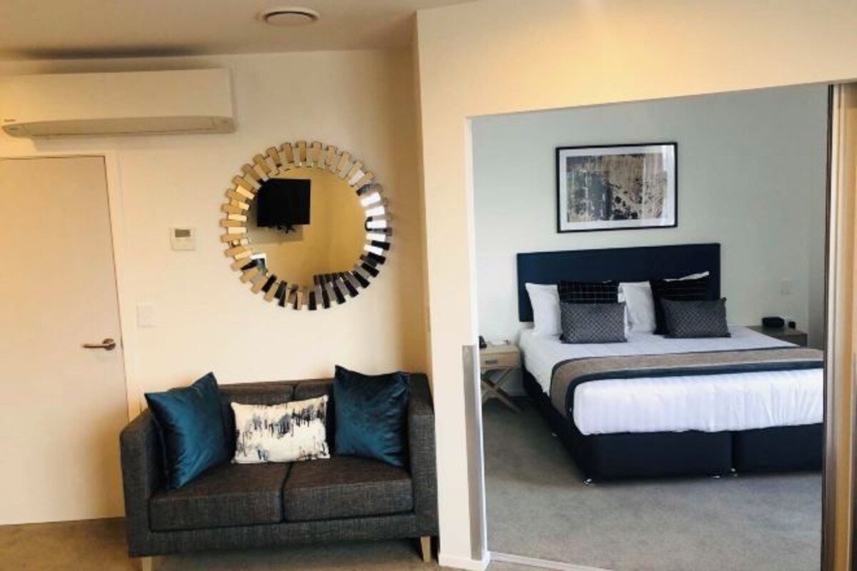 A room with a bed, a sofa, a wall-mounted TV, and a framed picture.