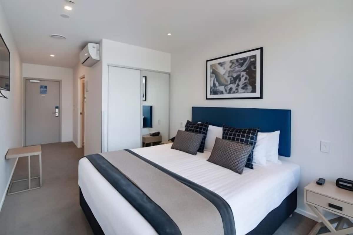 Ein modernes Hotelzimmer mit einem großen Bett, einem Nachttisch, einer Wand-Klimaanlage und einem gerahmten Kunstwerk über dem Bett.