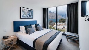 A modern hotel room with a large bed, a view of mountains and a lake, a small bedside table with a phone, and a TV mounted on the wall. - Ramada by Wyndham Queenstown Central (Queenstown)