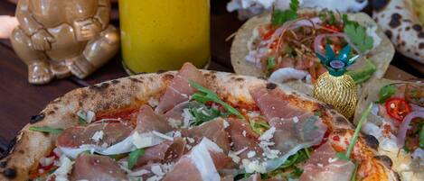 A variety of food items including pizzas and a drink, arranged on a wooden table.