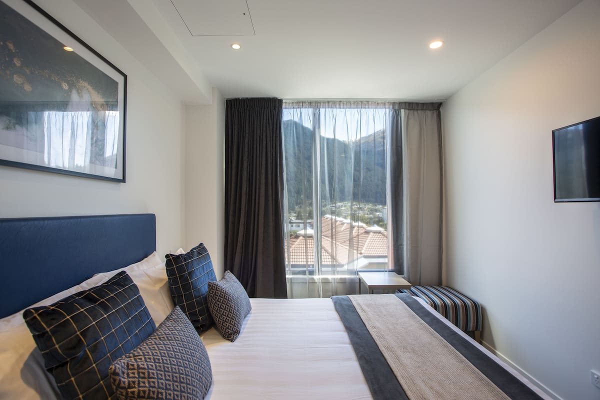 Ein Hotelzimmer mit einem großen Bett, Bergblick, Fernseher und einem Vorhangfenster.