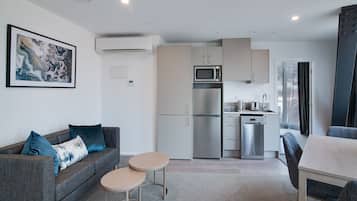 A modern kitchen with a microwave, refrigerator, and dishwasher. There is a gray sofa with blue cushions and a small round table.