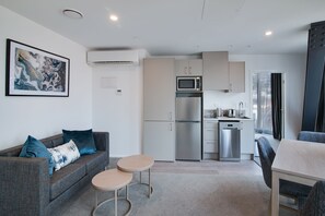 A modern kitchen with a microwave, refrigerator, and dishwasher. There is a gray sofa with blue cushions and a small round table.