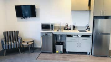 A compact kitchen with a microwave, sink, and refrigerator. A striped chair and a small round table are visible.