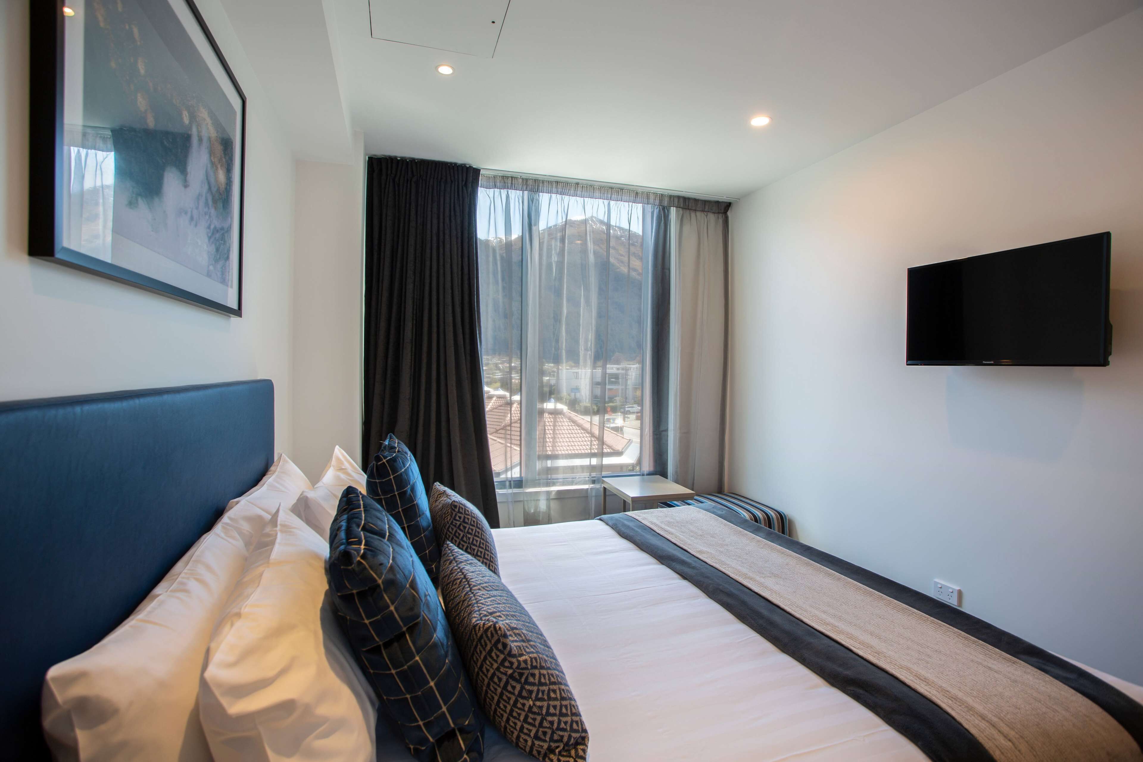 Habitación de hotel con una cama grande, un televisor de pantalla plana en la pared y una ventana con vistas a la montaña.