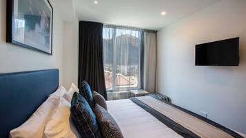 A hotel room with a large bed, a flat-screen TV mounted on the wall, and a window with a mountain view.
