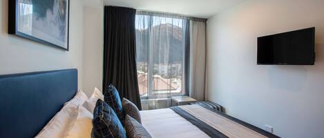 A hotel room with a large bed, a flat-screen TV mounted on the wall, and a window with a mountain view.
