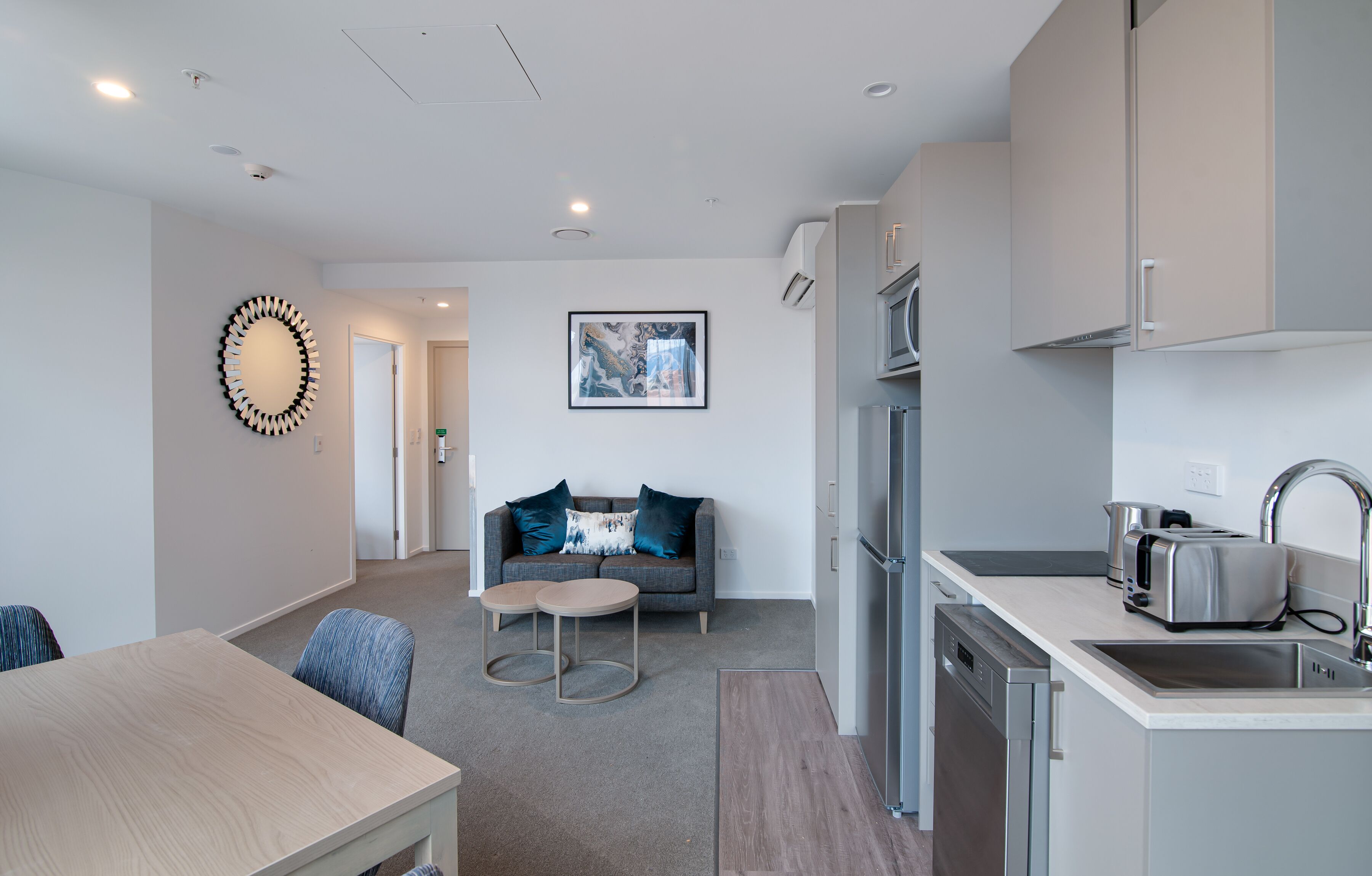 A modern kitchen with a built-in oven, a sink, and a toaster. There is a dining area with a table and chairs, and a living area with a sofa and a coffee table.