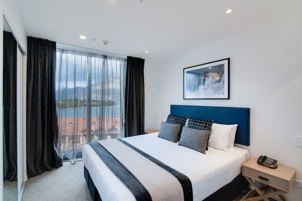 Ein Hotelzimmer mit einem großen Bett, Blick durch das Fenster und einem gerahmten Bild an der Wand.