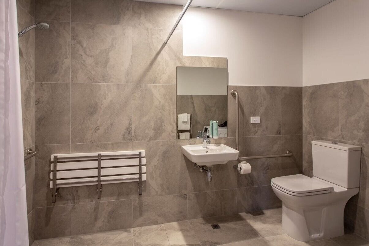 A modern bathroom with a shower, sink, toilet, and a handrail for accessibility.