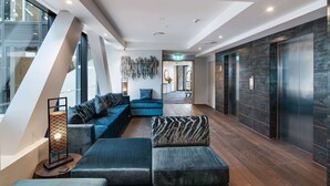 A modern lobby with a sectional sofa, a standing lamp, and a reception desk. - Ramada by Wyndham Queenstown Central (Queenstown)