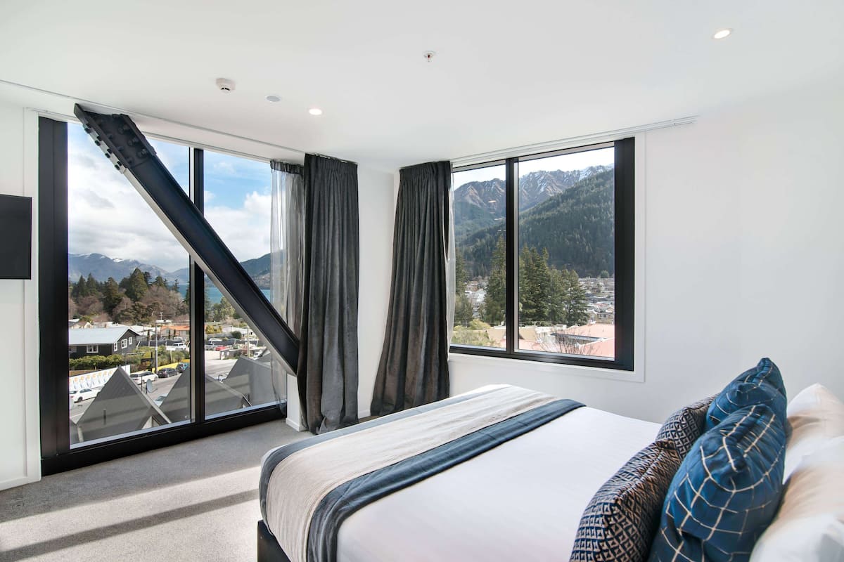 Ein Schlafzimmer mit einem großen Bett, Blick auf Berge und eine Stadtansicht durch große Fenster.