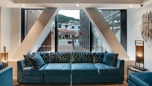 A modern living room with a large sofa, a view of the outside, and a geometric ceiling design. - Ramada by Wyndham Queenstown Central (Queenstown)