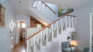 A modern interior with a wooden staircase, a dining area with a glass table, and a kitchen visible in the background. - Bajamar Nerja II 7 by Casasol (Nerja)