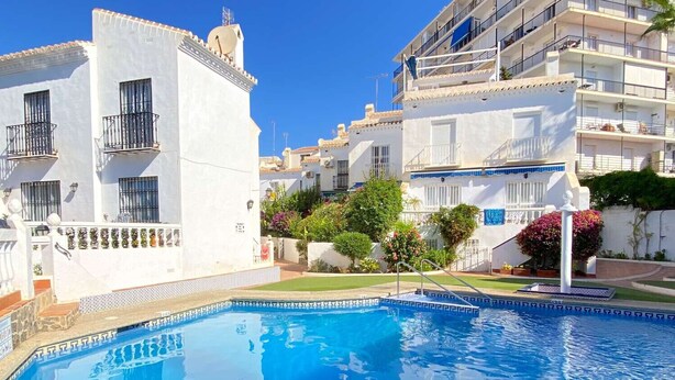 A swimming pool surrounded by white buildings with balconies, a clear sky, and some greenery. - Bajamar Nerja II 7 by Casasol (Nerja)