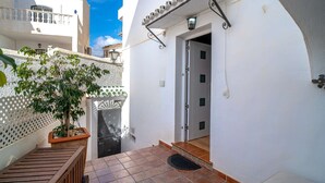 A narrow alleyway with a white building, a wooden bench, a potted plant, and a door leading to a balcony. - Bajamar Nerja II 7 by Casasol (Nerja)