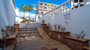 A courtyard with a tiled staircase leading to a balcony, surrounded by white walls and palm trees. - Bajamar Nerja II 7 by Casasol (Nerja)