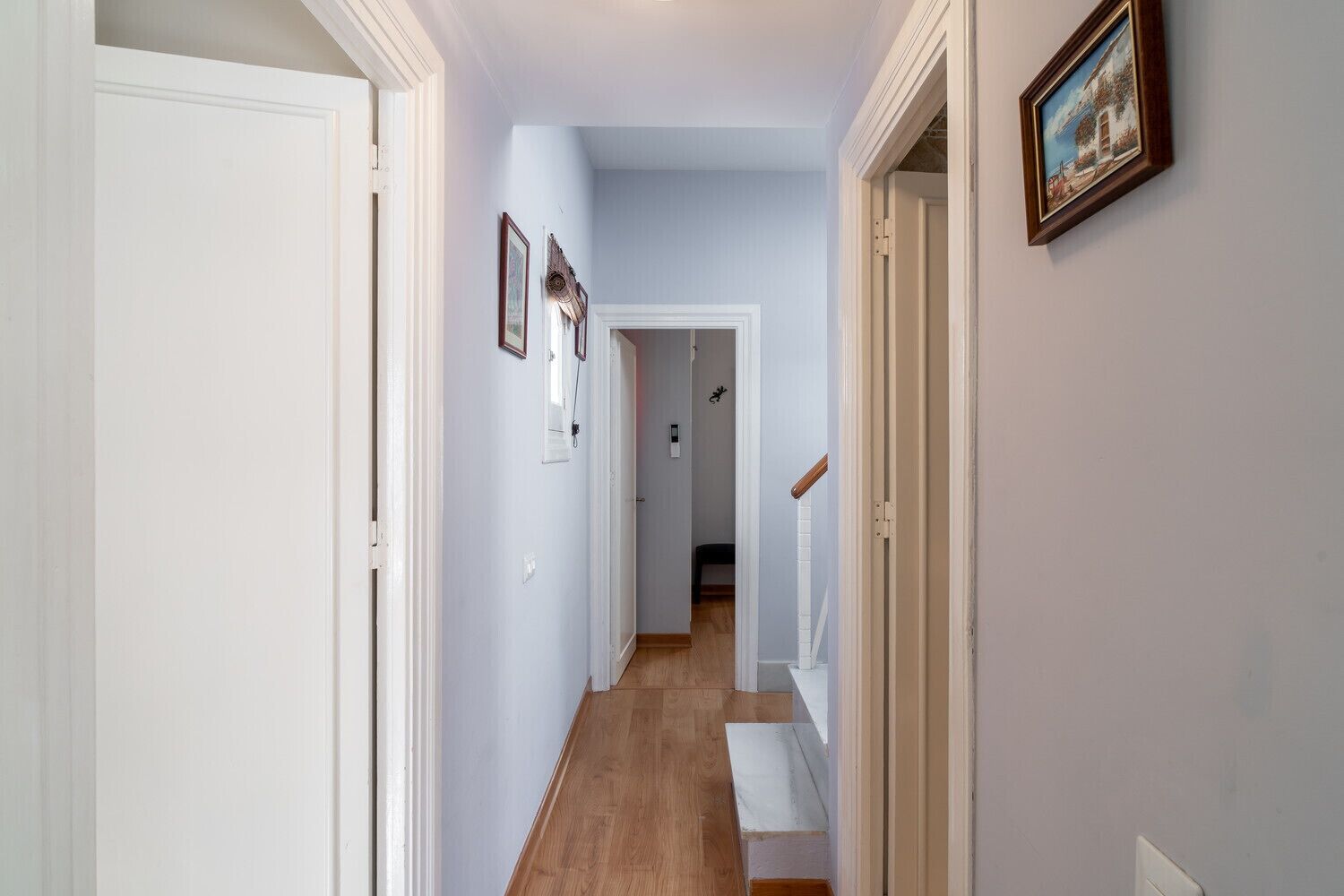 A hallway with white doors, a wooden staircase, and a framed picture on the wall.