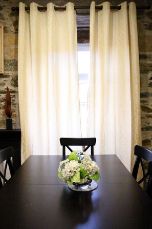 Ein Esstisch mit Blumen in einer Vase, schwarzen Stühlen und einer Steinwand mit Fenster und Vorhängen.