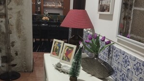 Una habitación con un aparador blanco, una lámpara roja, un pequeño árbol de Navidad y una ventana con baldosas estampadas.