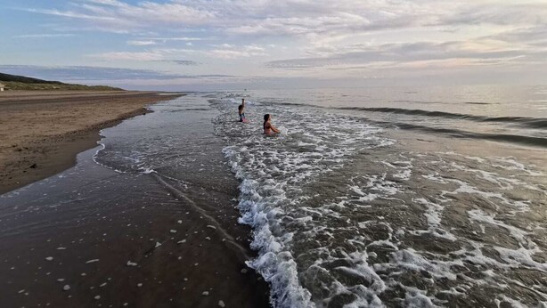Una playa con dos personas en el agua, una orilla de arena y un cielo despejado con nubes.