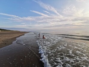 A beach with two people in the water, a sandy shore, and a clear sky with clouds. - Newly renovated house in Park De Kreek, Bruinisse (Bruinisse)