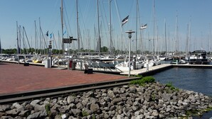 Un puerto deportivo con numerosas embarcaciones amarradas, un paseo marítimo de ladrillo rojo y una costa rocosa.