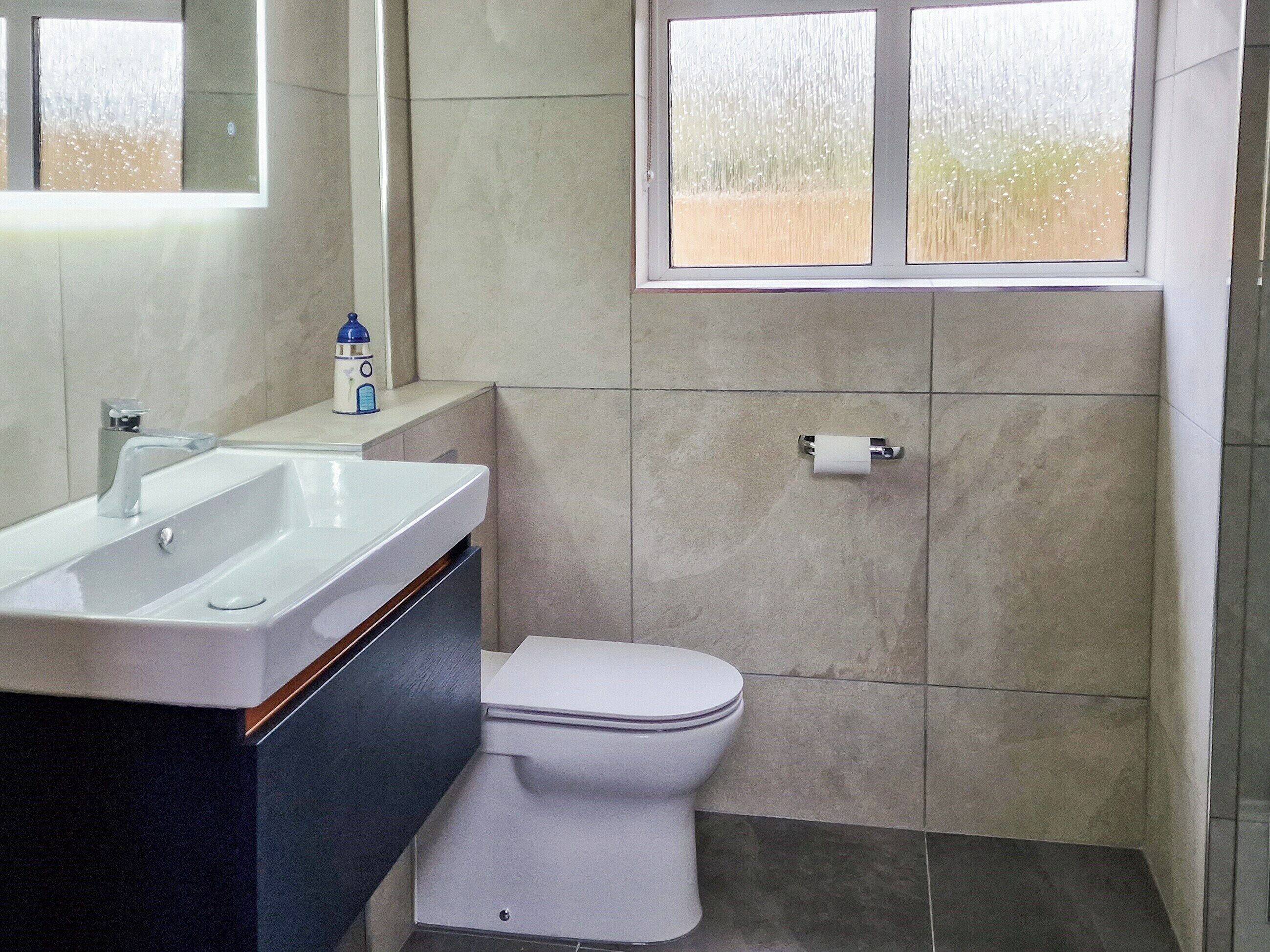 A bathroom with a sink, mirror, toilet, and window.