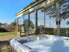 Un jacuzzi con cerramiento de vidrio, una silla de mimbre y un banco de piedra.