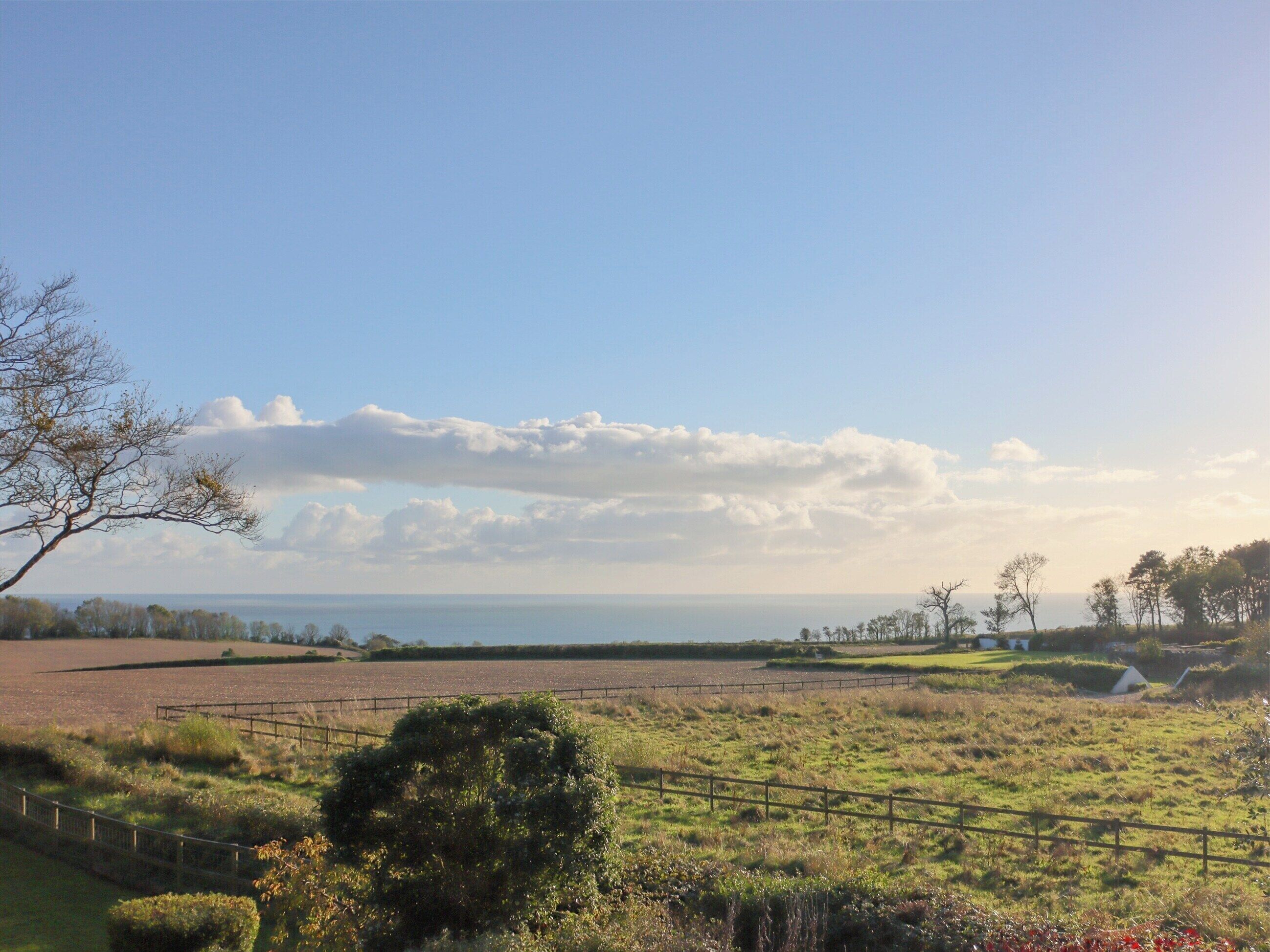 A rural landscape with fields, a fence, and a distant view of the sea under a clear sky.