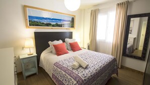 Una cama bien hecha con una colcha estampada, una lámpara de noche y un cuadro enmarcado sobre la cama.