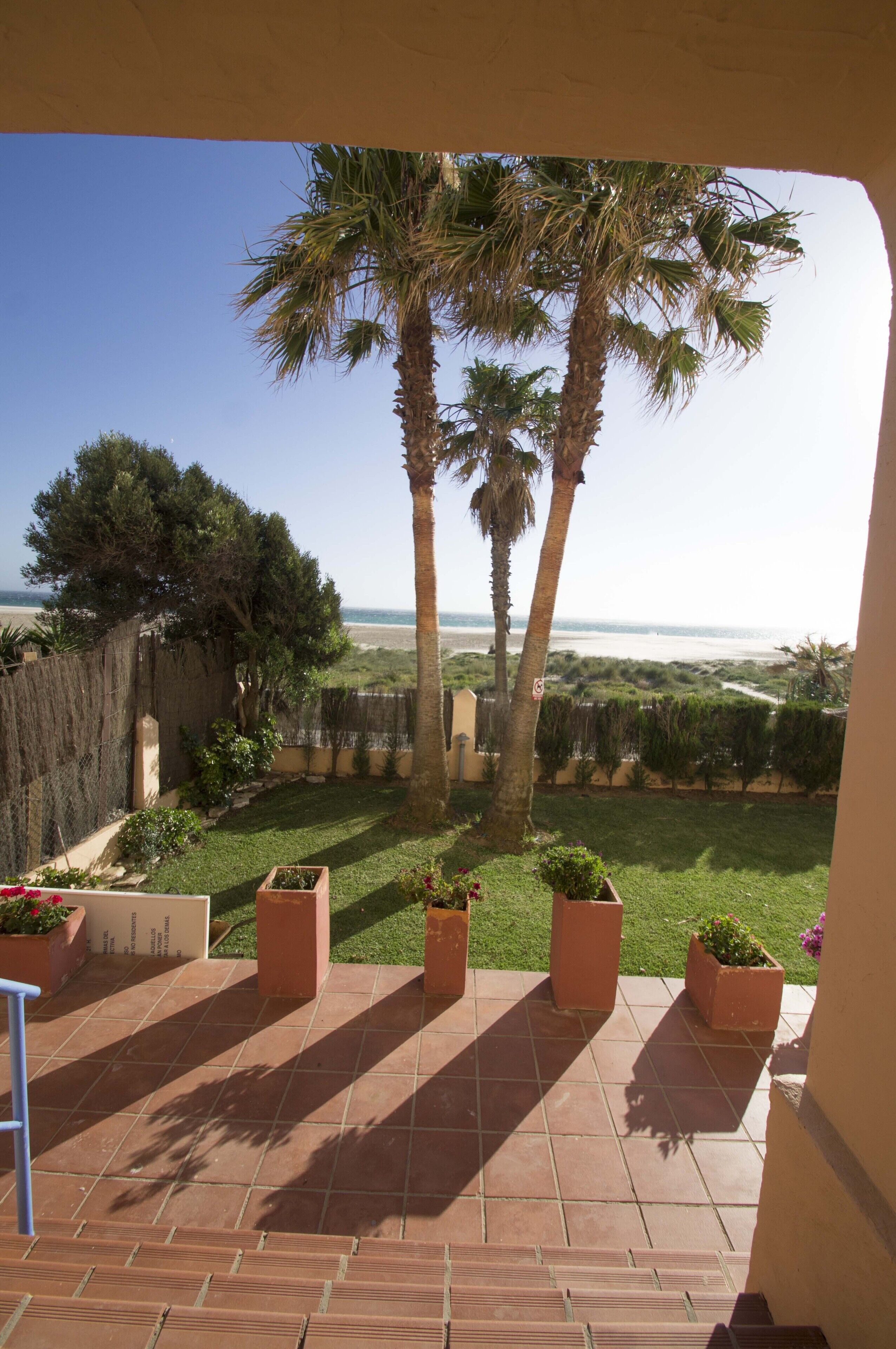 A terrace with a view of the beach, palm trees, and a tiled floor.