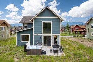A two-story house with a patio area featuring outdoor seating and a hot tub.