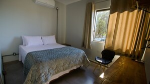 Une chambre à coucher avec un lit, une chaise, une fenêtre avec des rideaux et un bureau en bois.