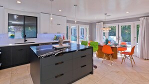 Una cocina moderna con una isla grande, armarios oscuros y un comedor con sillas de color naranja brillante.