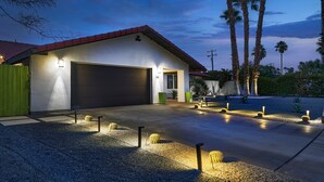 Una casa moderna con garaje, entrada para vehículos y un jardín bien cuidado con palmeras y cactus.