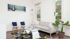 Un salon moderne avec un canapé blanc, deux fauteuils blancs, une table basse en verre et un grand tableau représentant une guitare.