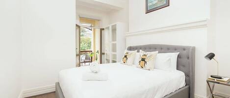 Un letto rifatto con un poggiatesta grigio, biancheria da letto bianca e cuscini decorativi.