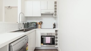 Une cuisine compacte avec des meubles blancs, un four encastré et un lave-vaisselle.