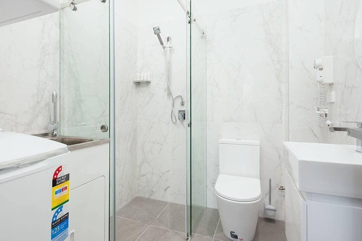 A modern bathroom with a glass-enclosed shower, a white toilet, and a sink with a marble countertop.