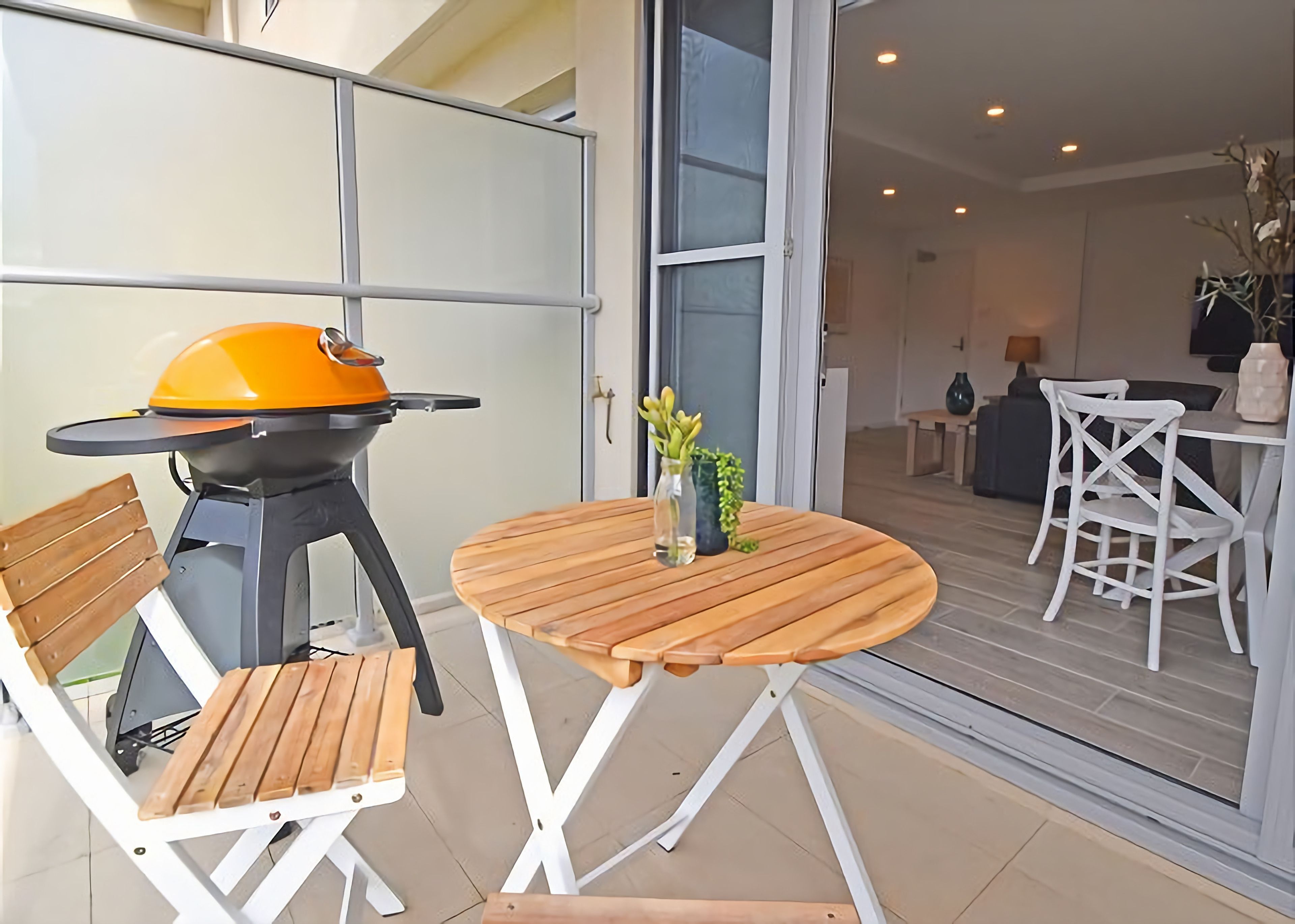 An outdoor patio with a barbecue grill, a round wooden table, and white folding chairs.