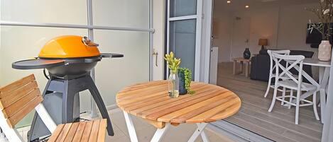 An outdoor patio with a barbecue grill, a round wooden table, and white folding chairs.