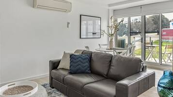 A modern living room with a leather sofa, a dining table, and a large window offering a view of the outdoors.