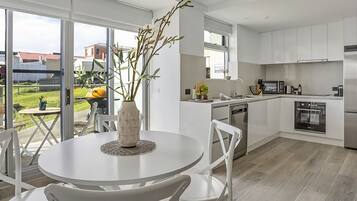 A modern kitchen with white cabinetry, a dining area with a round table and chairs, and a view of the outdoors through large windows.