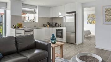 A modern kitchen with white cabinets, a stainless steel refrigerator, and a dining area with a leather sofa and a small table.