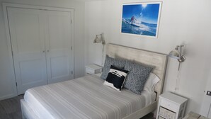 Ein aufgeräumtes Schlafzimmer mit einem großen Bett, zwei Nachttischen und einem an der Wand befestigten Bild.