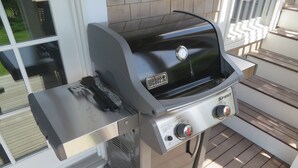 Ein Weber Spirit Gasgrill mit einem Beistelltisch auf einer Holzterrasse.
