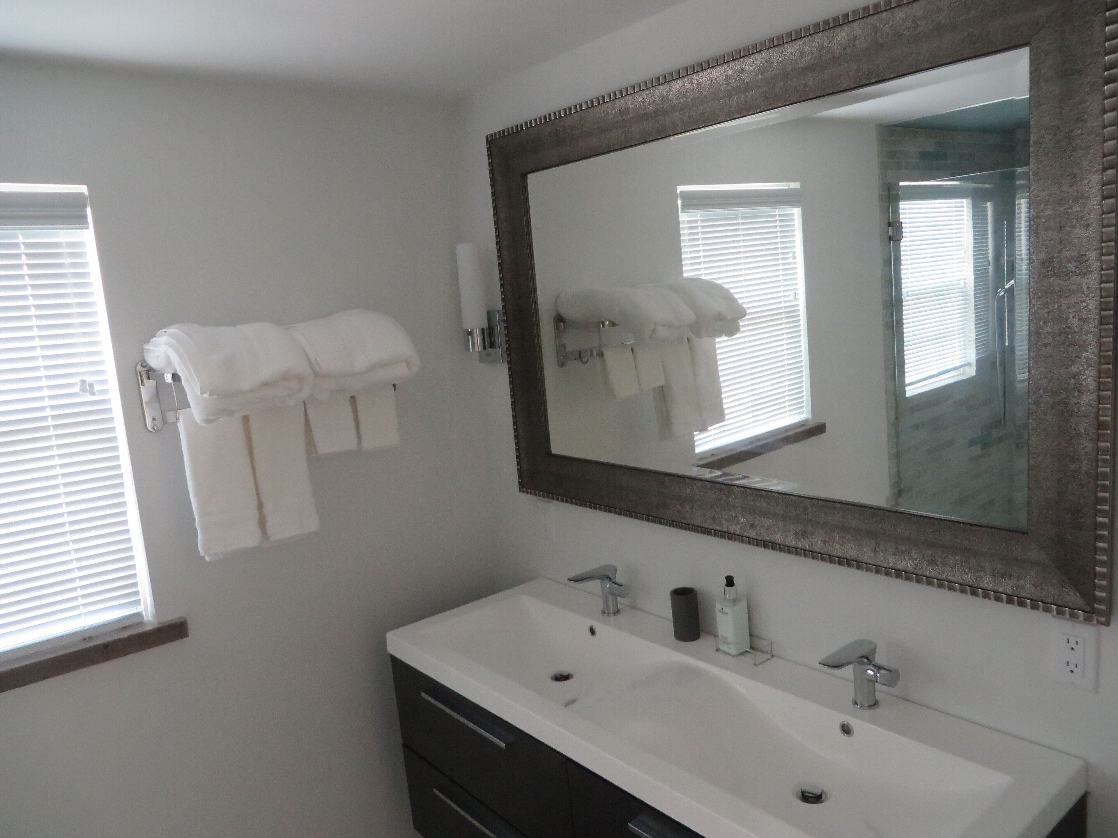 A bathroom with a white sink, two faucets, a large mirror, and towels hanging on a rack.
