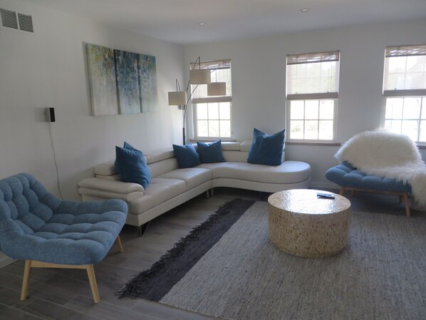 A modern living room with a white sectional sofa, a blue armchair, and a round coffee table. - Brand new modern 2 bedroom apartment (Nantucket)